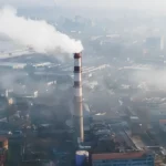 Chimenea industrial emitiendo humo en una zona urbana, ilustrando la necesidad de tecnologías avanzadas como quantum LiDAR para la detección precisa de emisiones de metano.