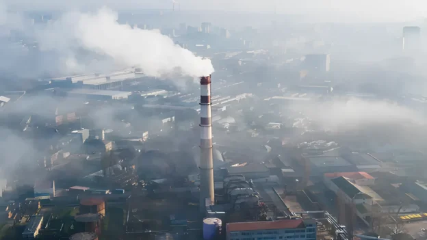 Chimenea industrial emitiendo humo en una zona urbana, ilustrando la necesidad de tecnologías avanzadas como quantum LiDAR para la detección precisa de emisiones de metano.