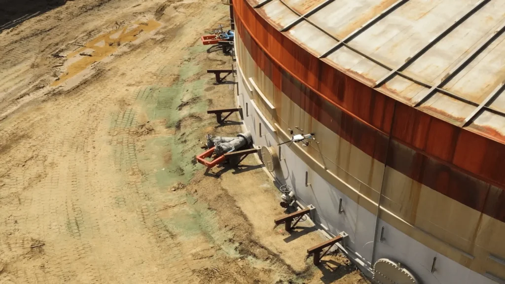 Drone performing a NDT inspection on a large industrial storage tank, showcasing a typical use case for space vs terrestrial hardware comparisons.