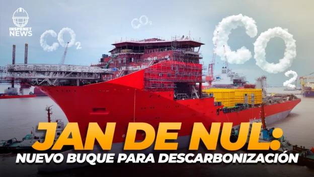 Buque rojo de gran tamaño en un astillero, en proceso de construcción, con letras en el cielo que forman “CO₂” y el texto sobreimpreso: “Jan De Nul: nuevo buque para descarbonización”.