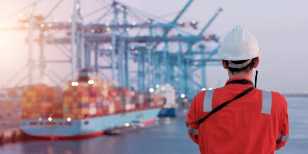 Maritime terminal operator supervising port maneuvers and operations in front of a container ship.