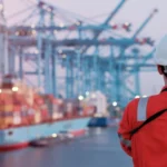 Maritime terminal operator supervising port maneuvers and operations in front of a container ship.