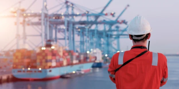 Maritime terminal operator supervising port maneuvers and operations in front of a container ship.