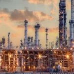 Petrochemical plant illuminated at dusk. Complex of pipes and industrial equipment that applies Risk-Based Inspection (RBI).