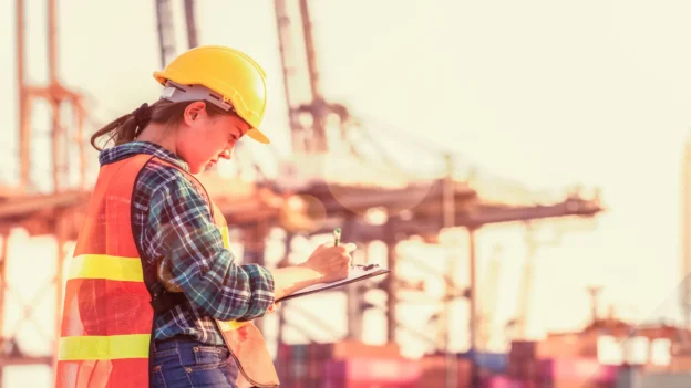 Port worker wearing a helmet and safety vest taking notes at a maritime terminal during a logistics operation, representing the Port of Cartagena.
