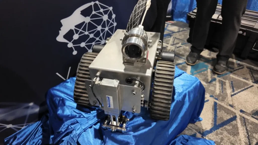 Robot PneuBot sobre una tela azul, con orugas de tracción y cámara frontal, exhibido durante un evento industrial.