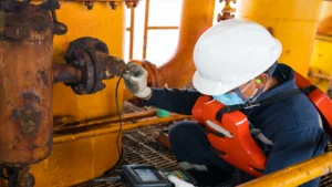 Inspector técnico realiza medición con equipo ultrasónico sobre una tubería corroída en una plataforma offshore, como parte de prácticas de control de corrosión.