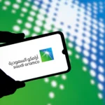 Logo de Saudi Aramco en un teléfono móvil con fondo corporativo azul y verde.