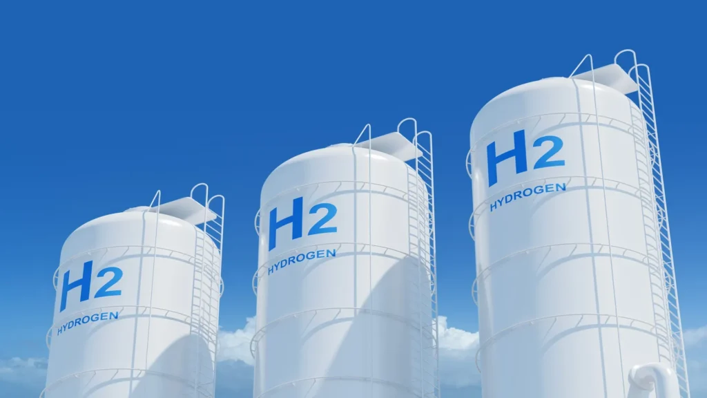 Tanques blancos de almacenamiento de hidrógeno etiquetados como "H₂", bajo un cielo azul despejado, simbolizando producción limpia y desarrollo energético sostenible.