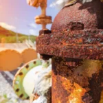 Tubería industrial con corrosión bajo aislamiento mostrando óxido severo y deterioro del metal en una instalación al aire libre.