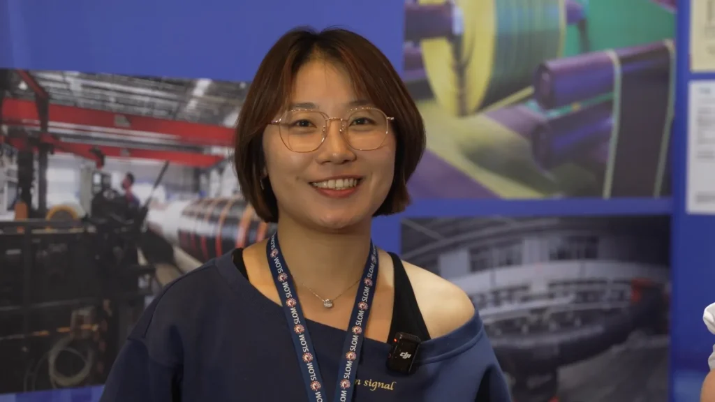 Wang Wei, ingeniera de ventas de VH-MARINETECH, sonríe durante el evento SLOM 2025 mientras presenta las soluciones de mangueras flotantes de la empresa.
