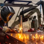 Welder performing a joint on a metal surface, wearing protective gear, with sparks flying—preparation stage before applying cadmium coating for corrosion protection.