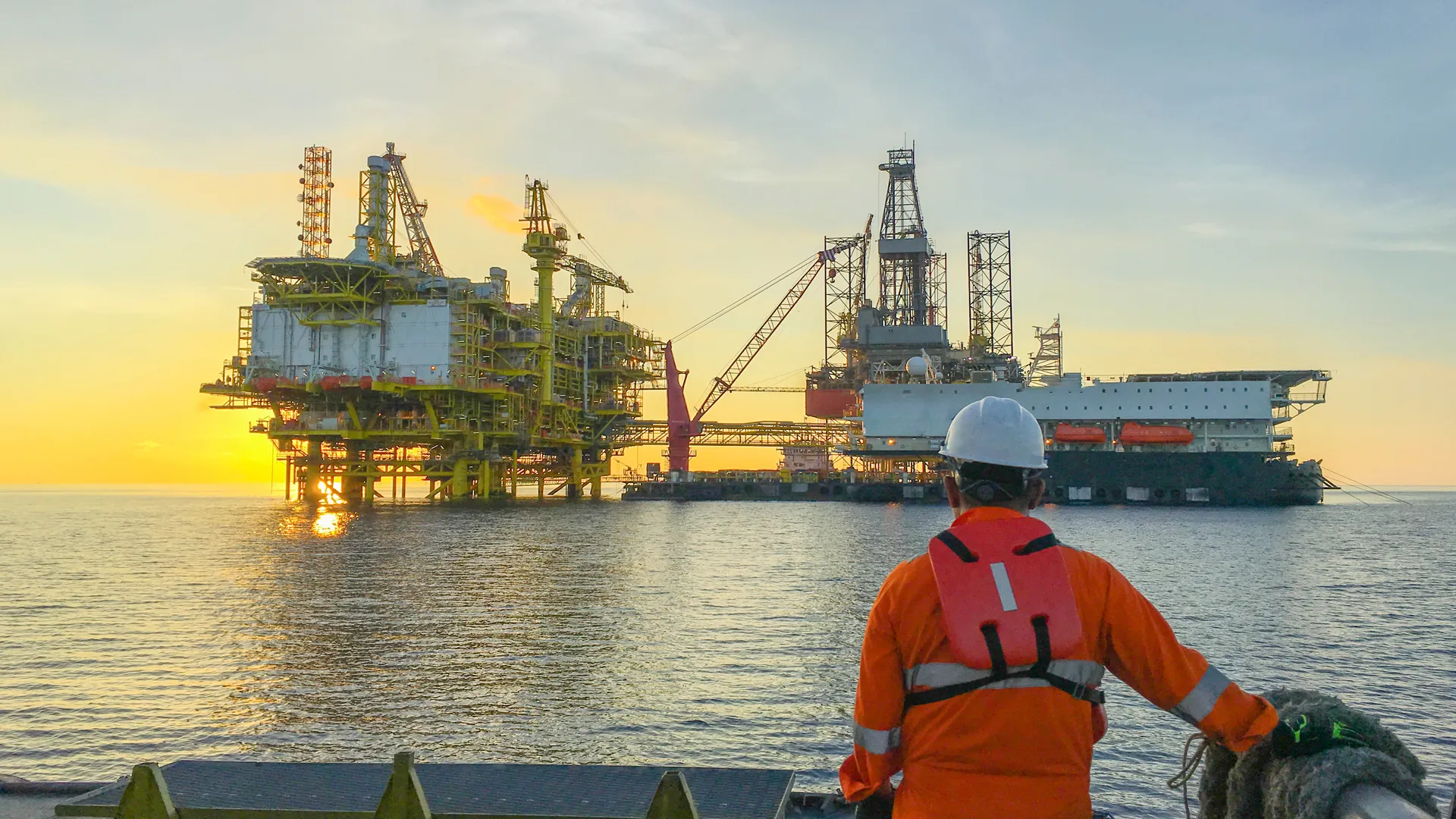 Worker observing offshore platforms in operation during sunrise.