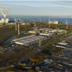 Wind energy en Europa con aerogeneradores junto a instalaciones industriales y la costa.