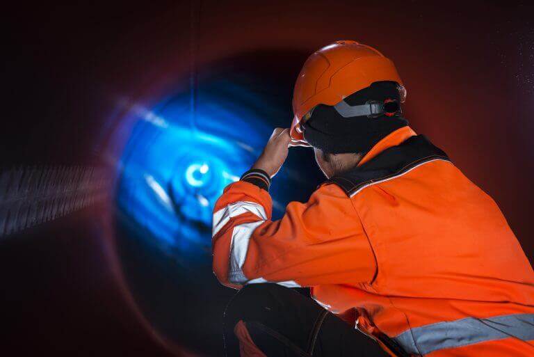 Pipeline construction worker in reflective protective uniform inspecting pipe tube for natural gas distribution